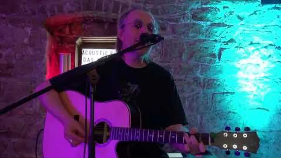 Peter Hefner mit Akustikgitarre am Mikrofon in einem Gewölbe aus Bruchstein, farbig ausgeleuchtet