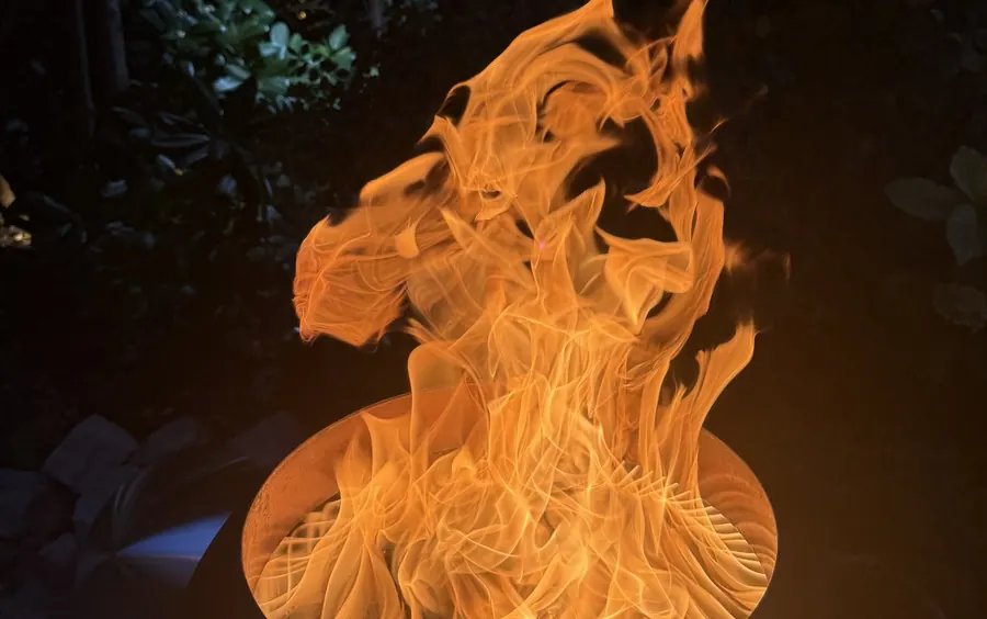Nahaufnahme der brennenden Feuerschale von oben: die Flamme dreht sich im Korb, am Rand der Lochkranz