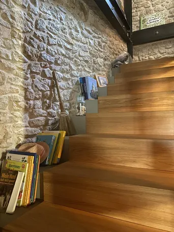 Die Treppe an der Bruchsteinwand — Eiche auf Stahl, Stufen als Ablage: der Aufgang gehört zum Raum.