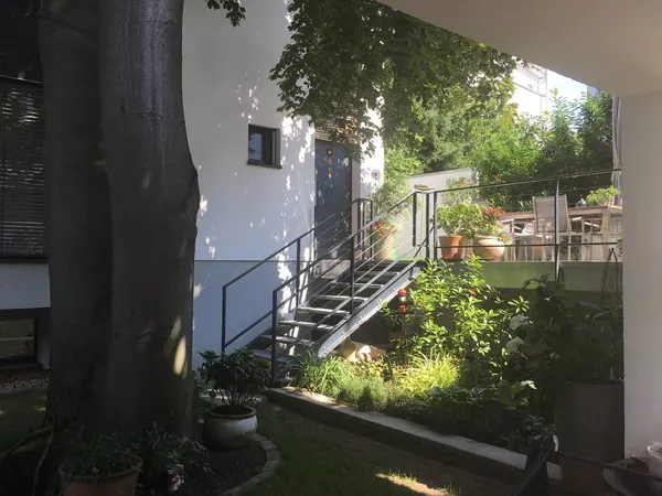 Der Weg in den Garten — Eine Stahltreppe führt von der Terrasse hinunter; im Vordergrund der Stamm einer alten Buche.